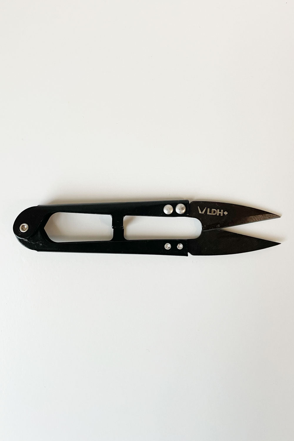 One thread snips lying horizontally. The handles are slightly shiny and black; the blades are dark grey. LDH logo on the top blade. 