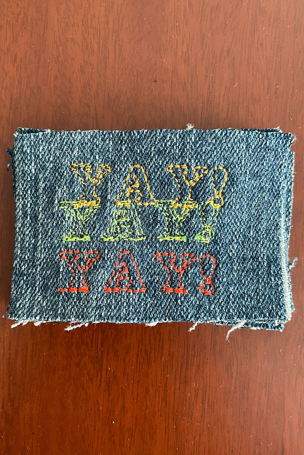 Triple YAY! embroidered patch on denim with orange, neon green, and cherry red embroidery thread. 