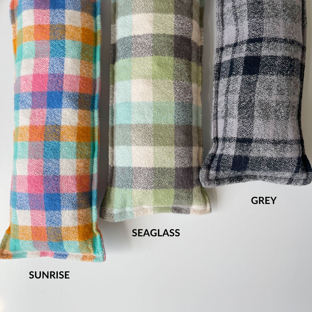 3 cherry pit warmers in plaid, from left to right with text: Sunrise: small plaid with pinks, oranges, blues, and teal greens. Seaglass: larger plaid with greens, light blue, and grey. Grey: small plaid with greys and black. 