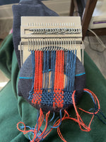 Load image into Gallery viewer, A 21-hook darning loom threaded with orange and blue thread. 
