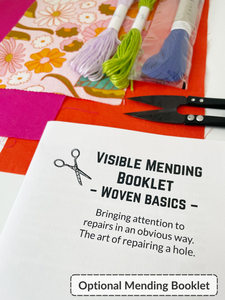 Paper booklet in foreground with text: Visible mending booklet-woven basics- bringing attention to repairs in an obvious way. The art of repairing a hole. Bright pink, orange, and 70's floral fabric scraps with light purple and green embroidery thread, dark blue sashiko thread, and black thread snips in the background. 