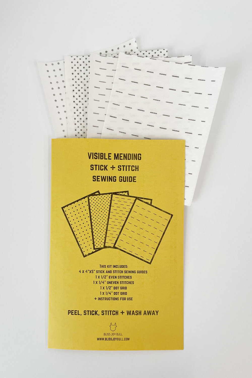 A piece of yellow paper folded in half with 4- 1/4 sheets of stick and stitch guides stick out of the top. The guides have grids, even , and uneven stitch guides. The yellow paper says: visible mending stick and stitch sewing guide, peel, stick, stitch, and wash away and contents of kit. Instructions are included. 