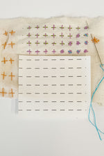 Load image into Gallery viewer, A mending sampler of plus and star stitches with a piece of stitching guide attached and stitches sewn on the guide. A few stitches are sewn without the guide and aren&#39;t as even. A cut piece of the guide sits on top of the sampler with a threaded needle inserted into the fabric. 
