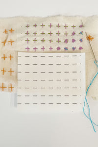 A mending sampler of plus and star stitches with a piece of stitching guide attached and stitches sewn on the guide. A few stitches are sewn without the guide and aren't as even. A cut piece of the guide sits on top of the sampler with a threaded needle inserted into the fabric. 