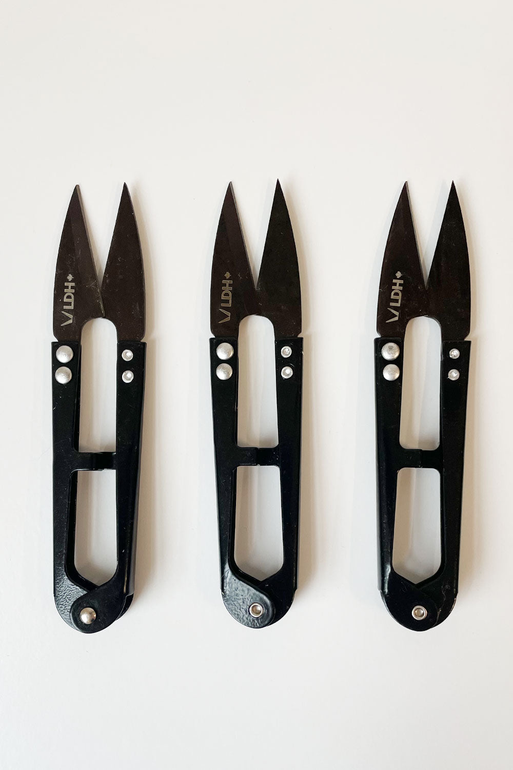 3 thread snips aligned vertically. The handles are slightly shiny and black; the blades are dark grey. LDH logo on the left blade. 