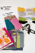 Load image into Gallery viewer, Assortment of mending supplies: Visible mending booklets for knit and woven fabrics made from paper. 2 sashiko threads, 2 embroidery threads, 2 needlepoint crewel wool cards, thread snips, needles and pins on cotton twill tape, and small assortment of cotton and denim fabric scraps. 
