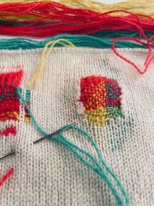 Visible mending/ darning repair in green, red, yellow on knit fabric
