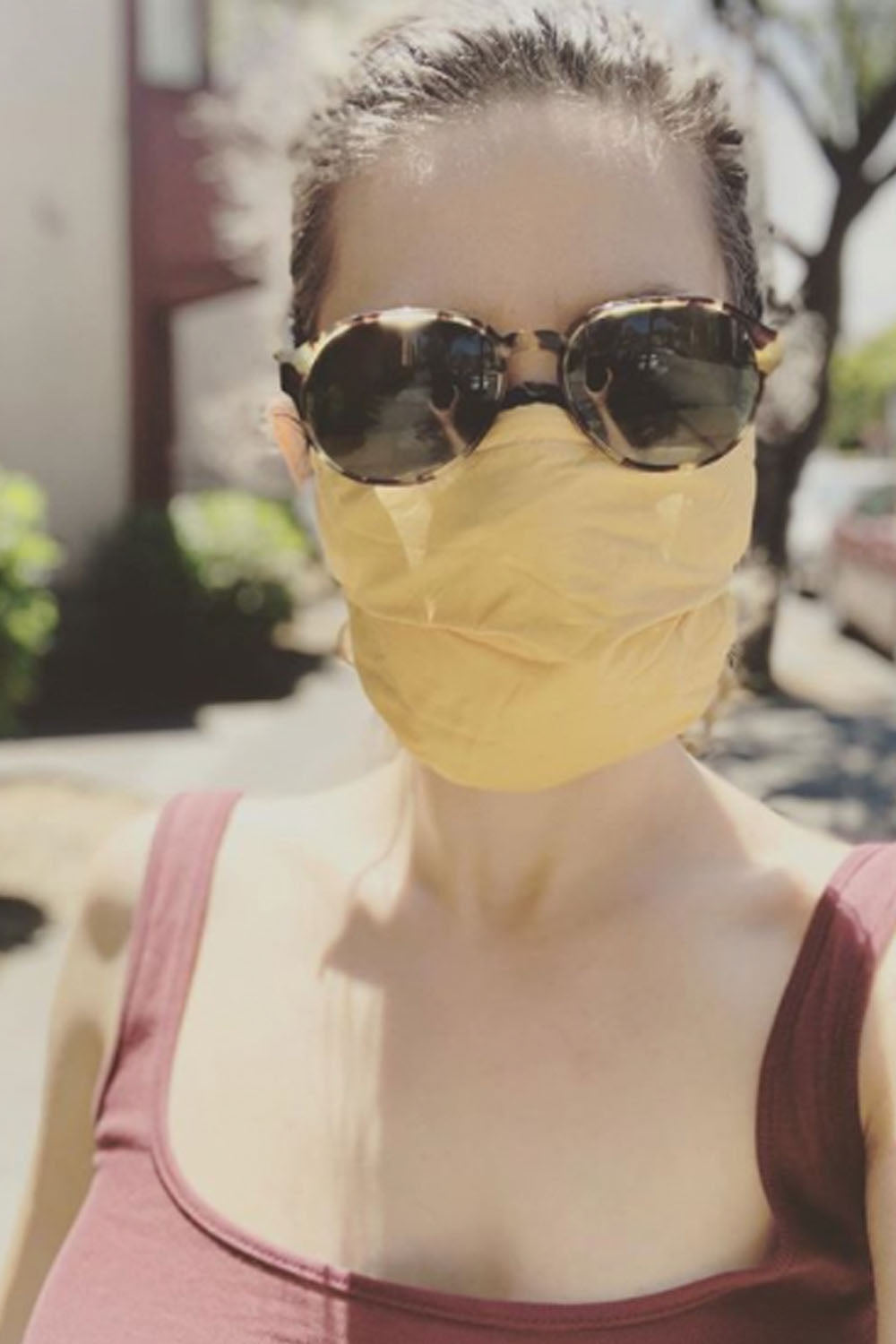 Woman in sunglasses and tank top wears light orange fabric face mask.