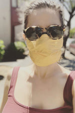 Load image into Gallery viewer, Woman in sunglasses and tank top wears light orange fabric face mask.

