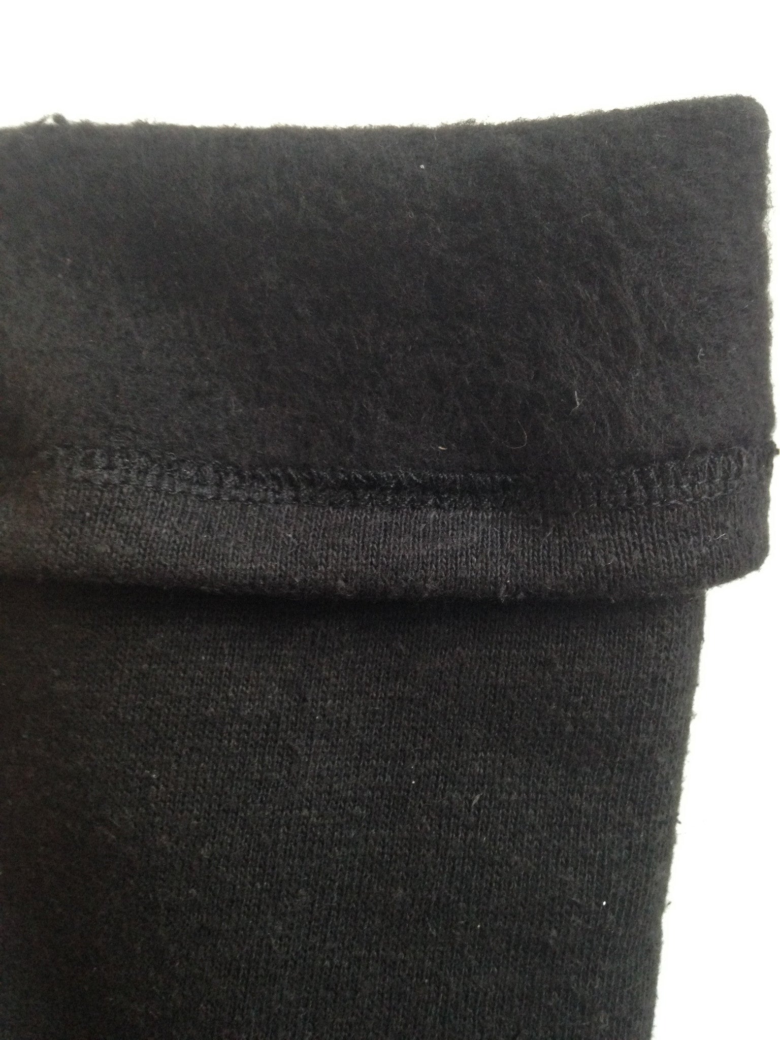 A close up of the inside of black fleece leg warmers shows the inside texture to be fuzzy. The outside texture is a smooth knit fabric. 