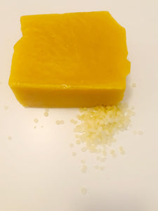 A small pile of beeswax pellets sits next to a block of beeswax on a white background. 