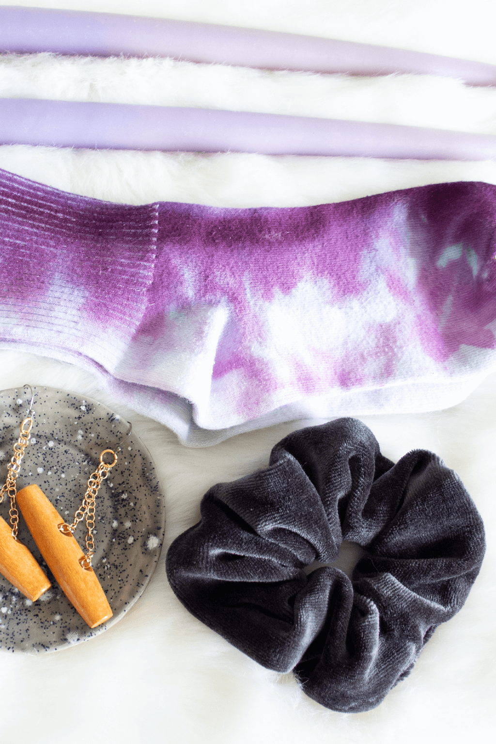 Black velvet scrunchie, purple dyed socks, wood earrings, and a pair of purple candles rest on faux fur. 