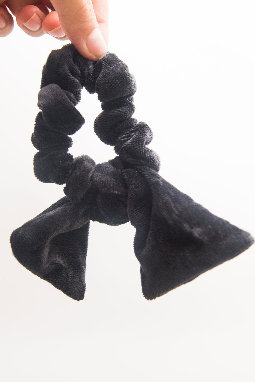 a black velvet bow hair scrunchie is held up by two pinched fingers