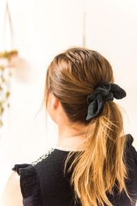 Woman faces away from camera. Her hair is tied in a mid-ponytail with a black velvet bow hair scrunchie.