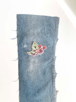 Load image into Gallery viewer, Cut denim leg with machine embroidered rose bush patch on the knee. 
