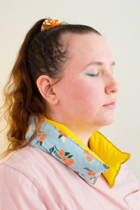 Profile of a woman with eyes closed wears a long and skinny cherry pit grain bag around her neck.