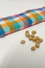 Load image into Gallery viewer, Close up of a plaid cherry pit filled eye pillow. A small pile of dried cherry pits are next to it. 
