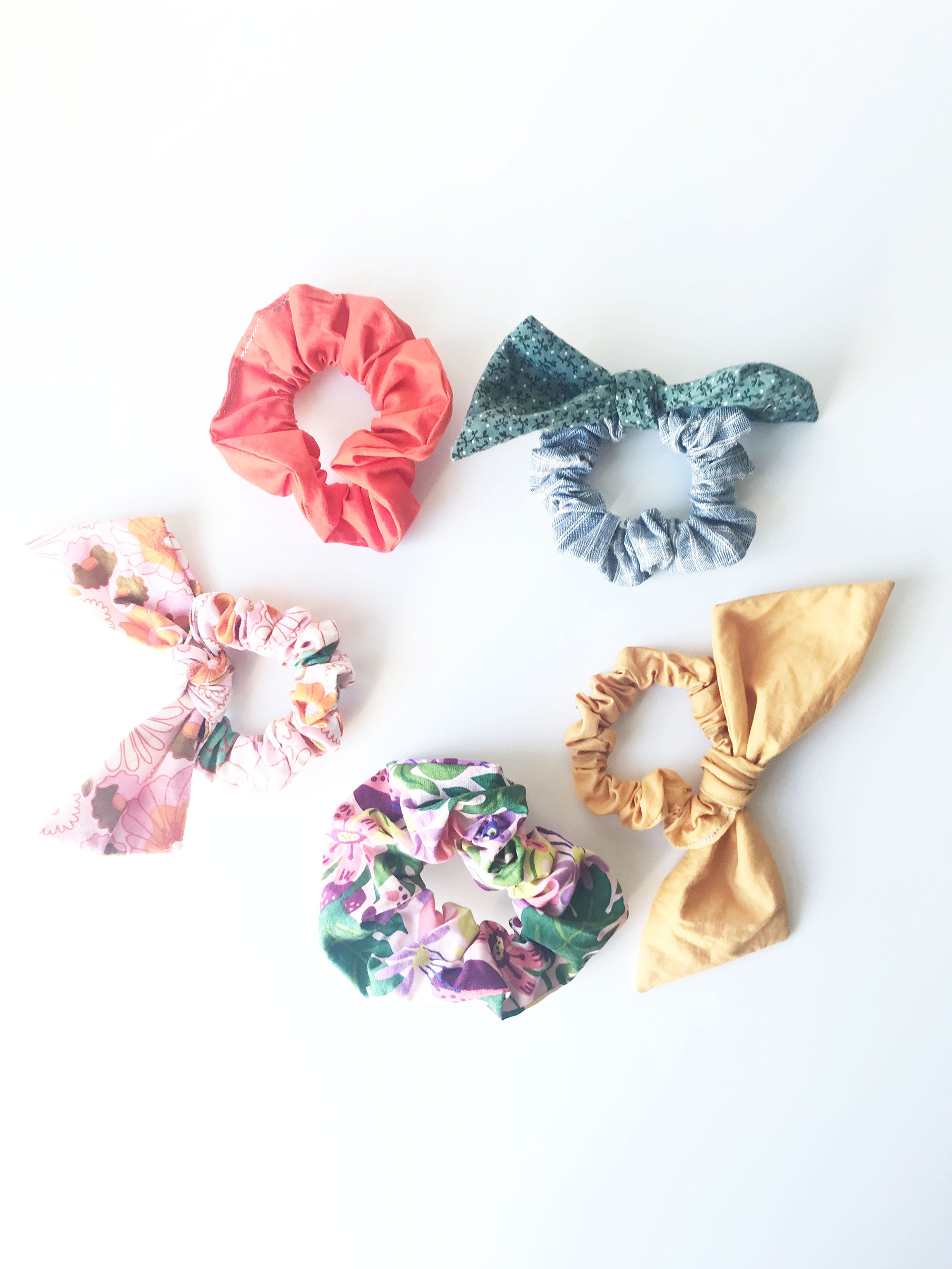 A circle of 5 classic and bow hair scrunchies sit on a white background. 