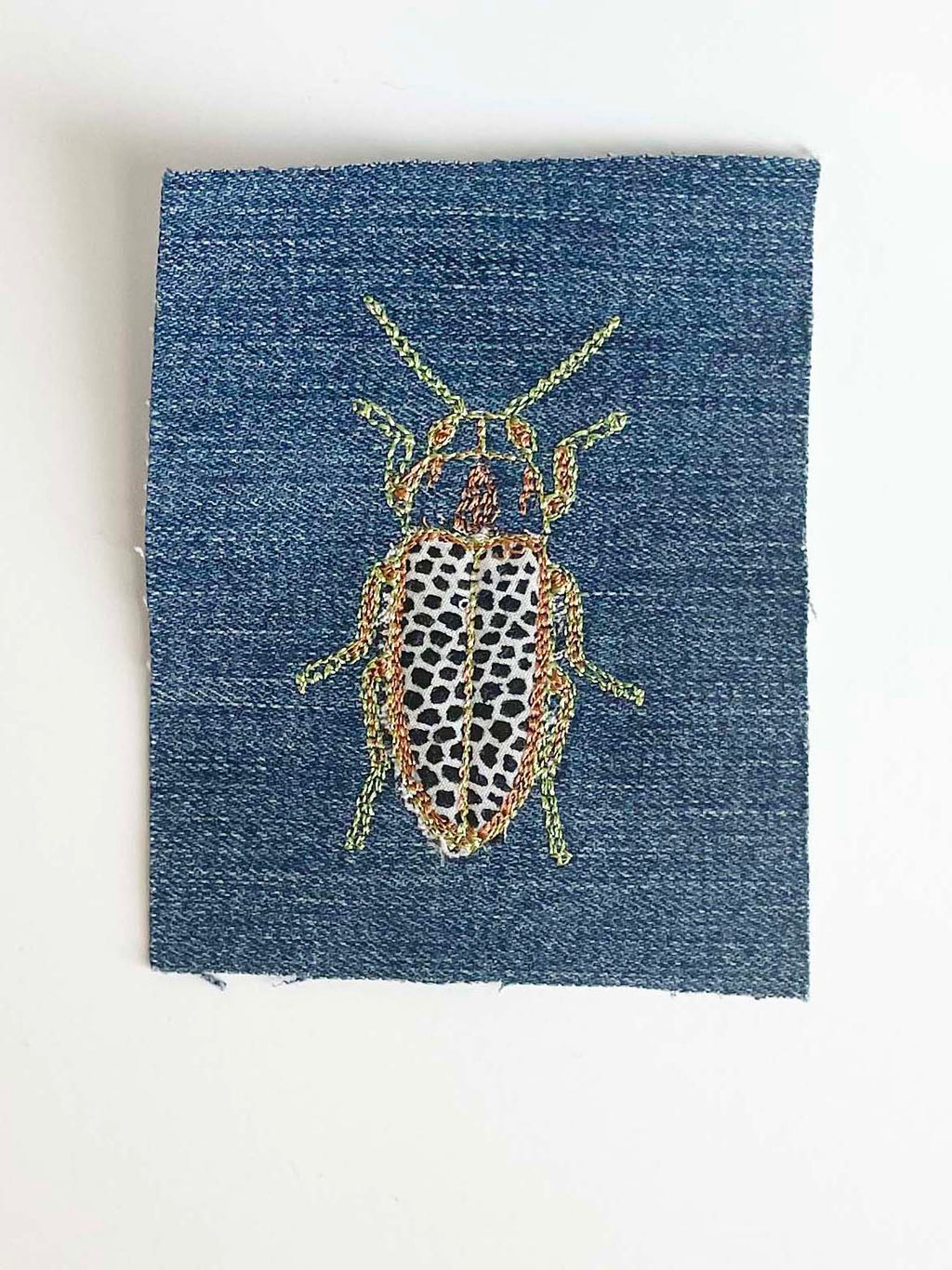 Machine embroidered beetle on denim swatch. 