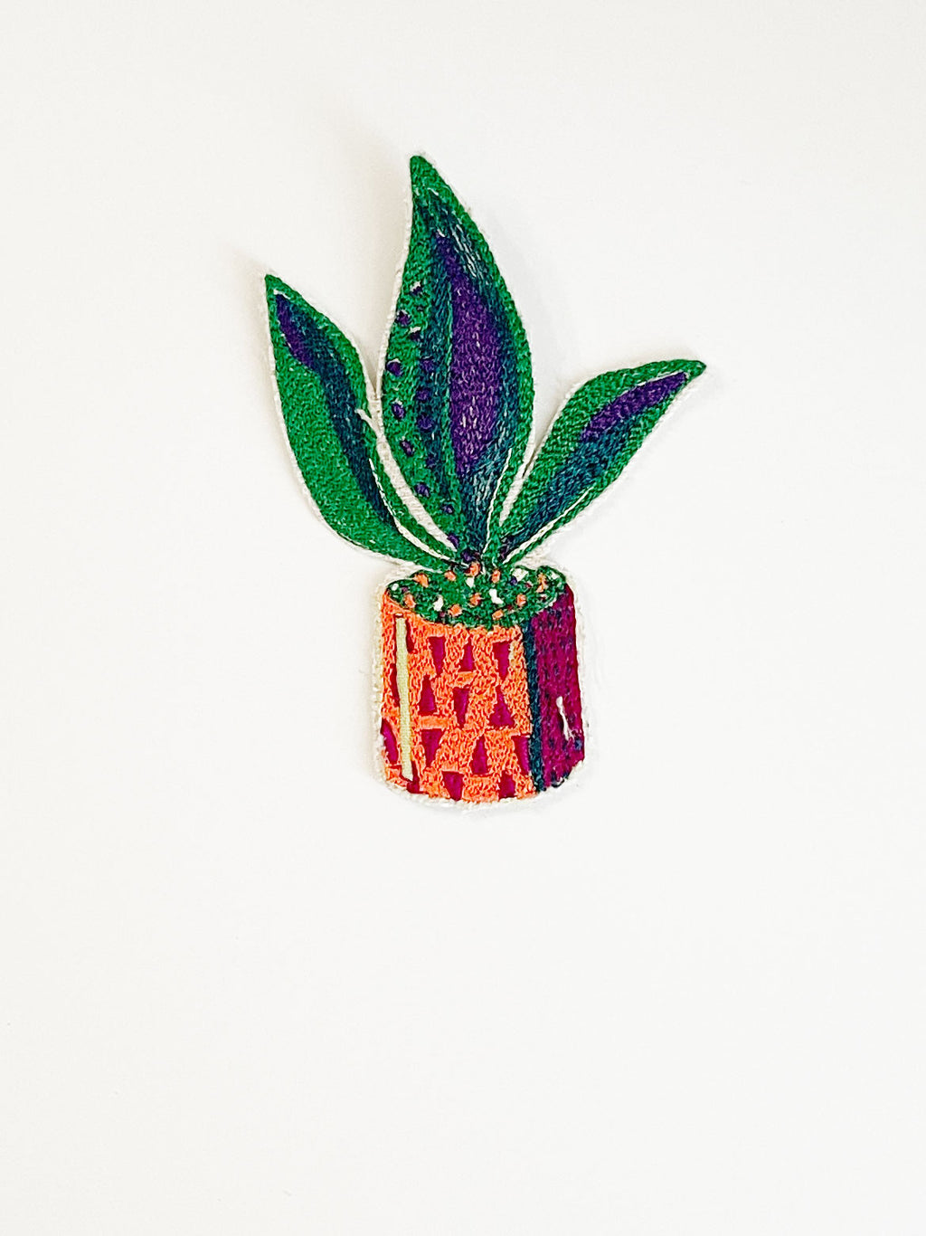 Machine embroidered snake plant in a pot iron-on patch. Plant pot in shades of red and orange. Plant is green, dark green, and purple. 