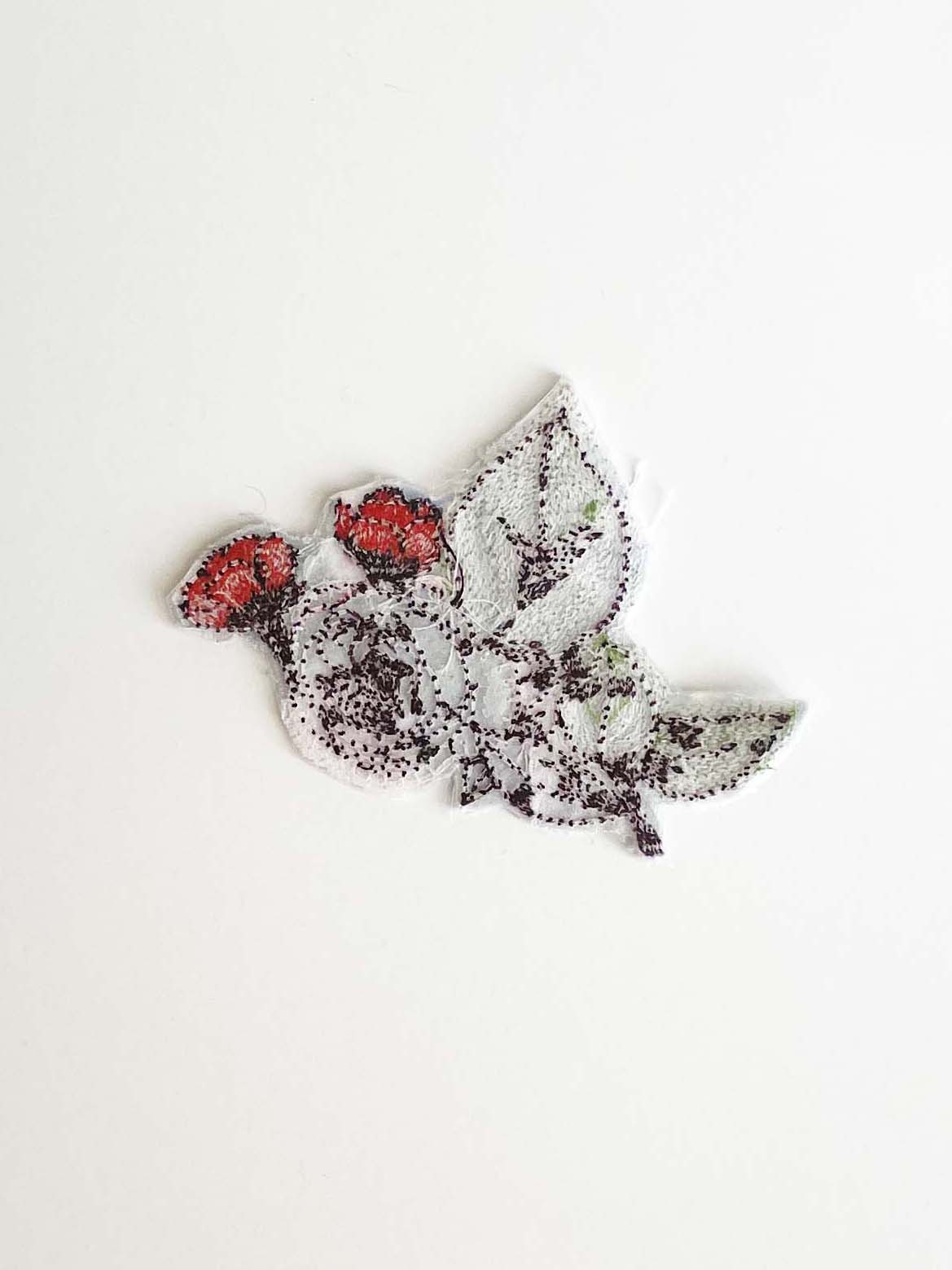 Back of embroidered rose bush shows clear adhesive backing with threads showing through. 