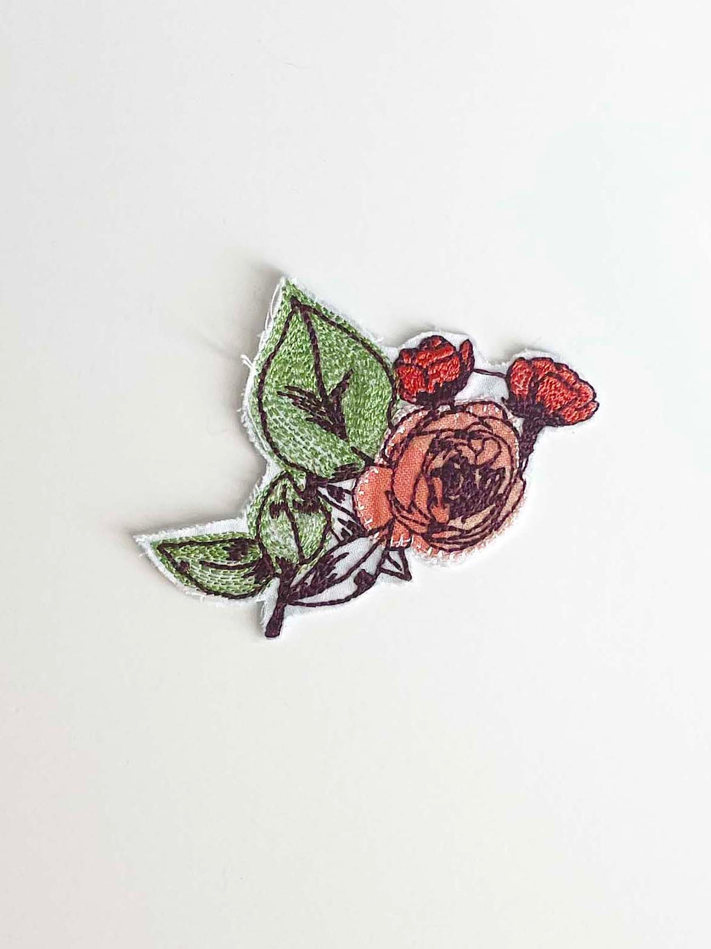 Machine embroidered rose bush in shades of burnt orange, burgundy, and bright green Upcycled ombre peach fabric completes the flower. 
