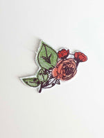 Load image into Gallery viewer, Machine embroidered rose bush in shades of burnt orange, burgundy, and bright green Upcycled ombre peach fabric completes the flower. 
