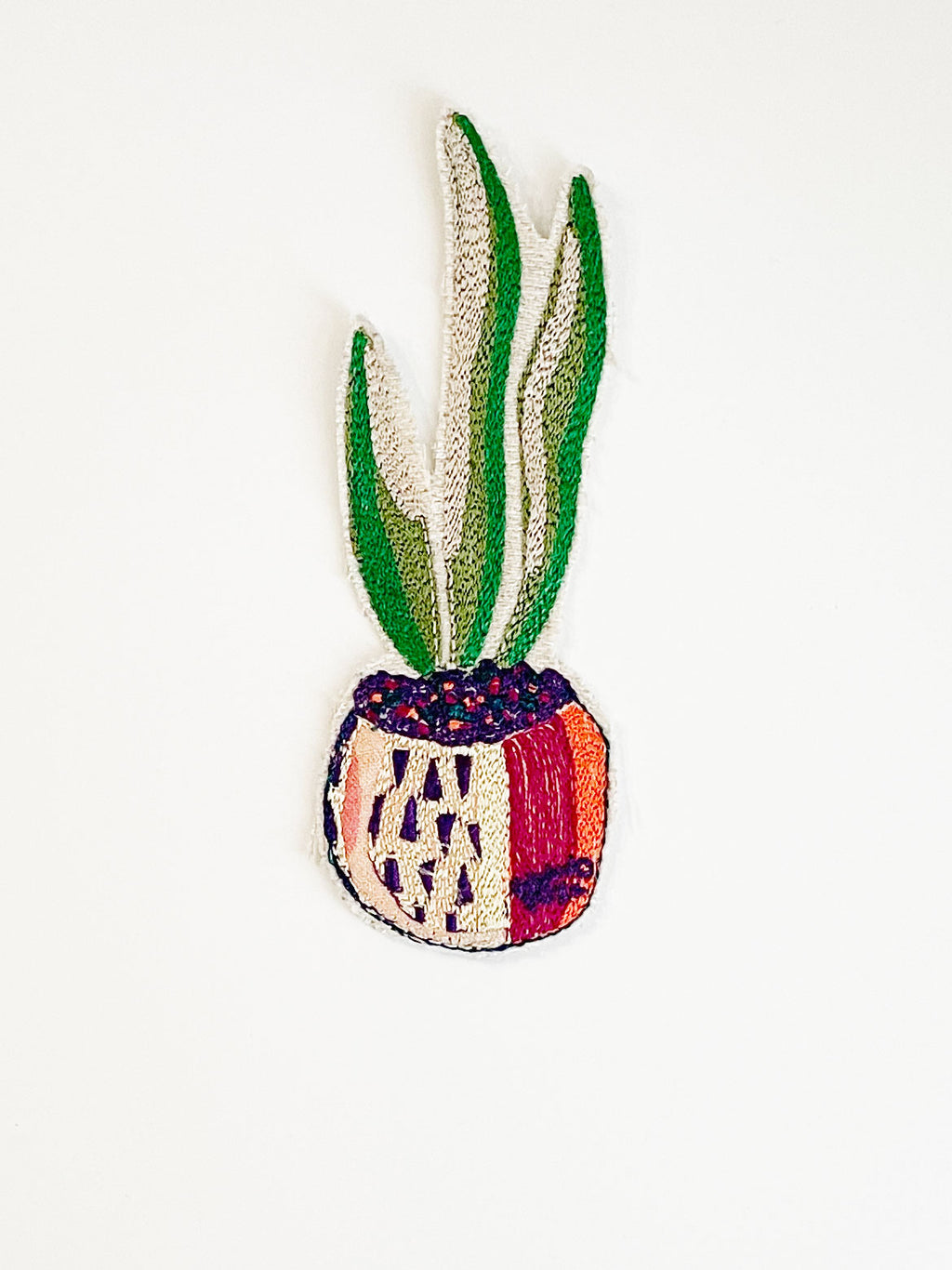 Machine embroidered snake plant in a pot iron-on patch. Plant pot in shades of red, orange, peach, and purple. 