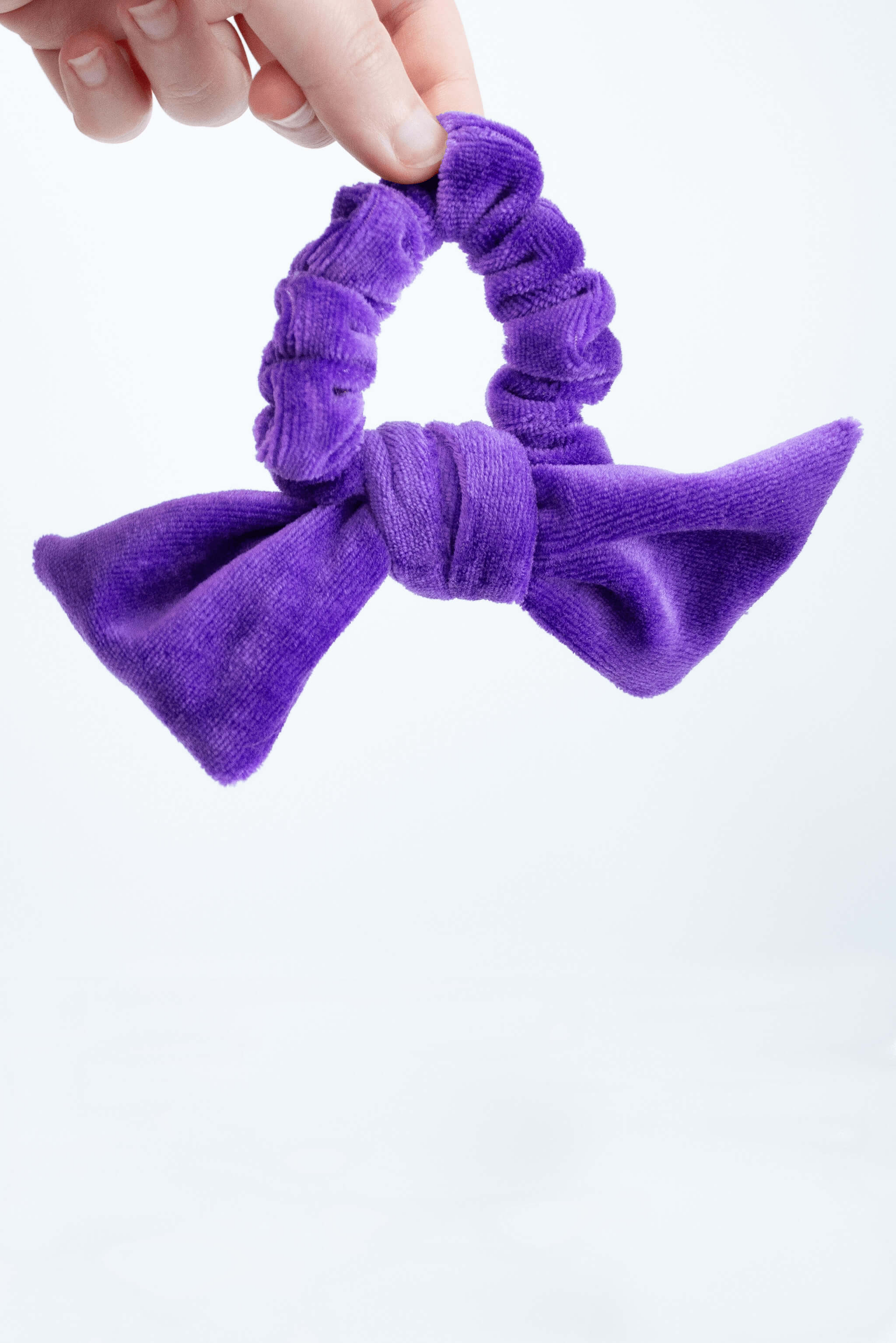 a black velvet bow hair scrunchie is held up by two pinched fingers