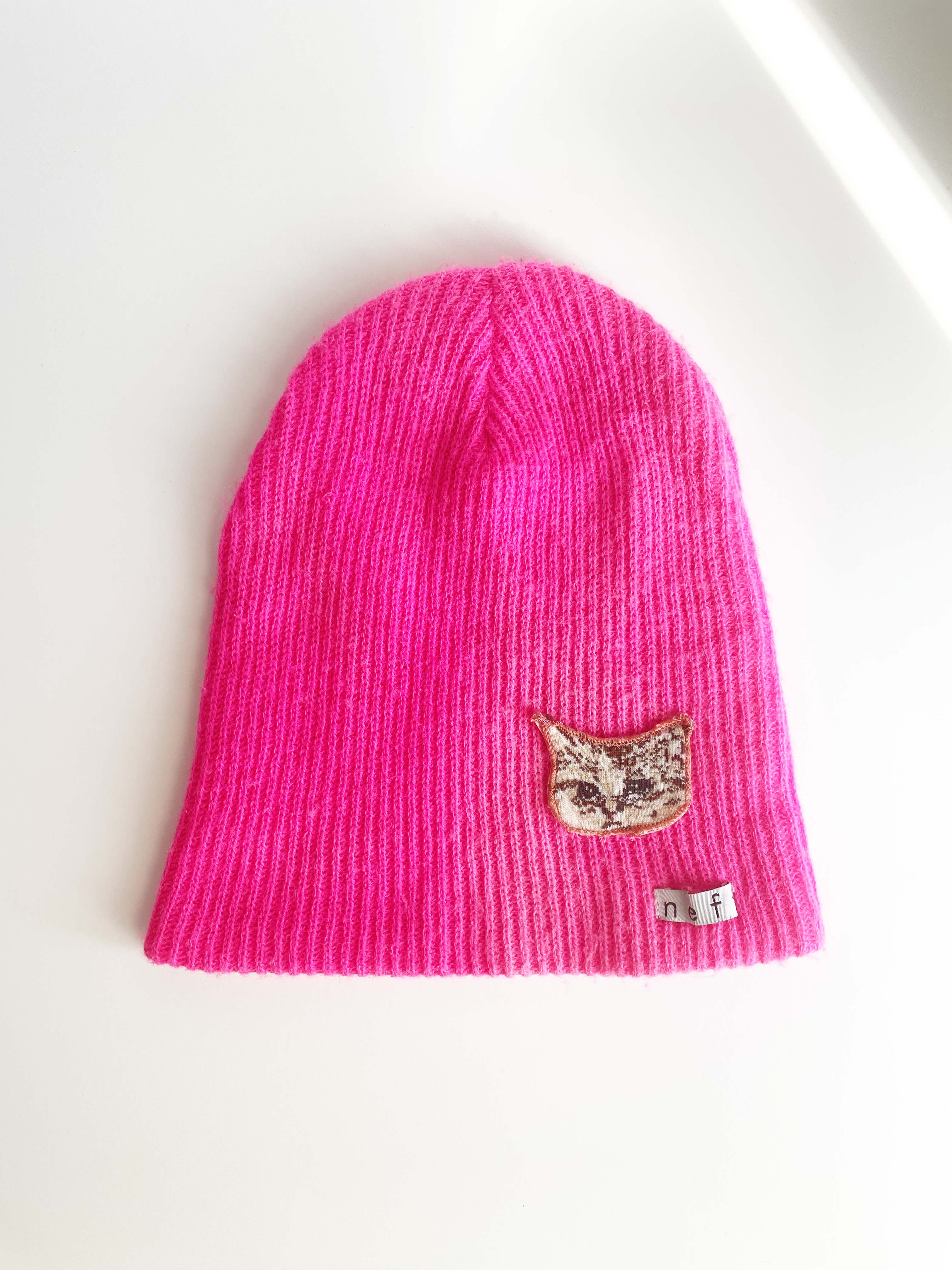 Sad cat head applique on hot pink knit hat.