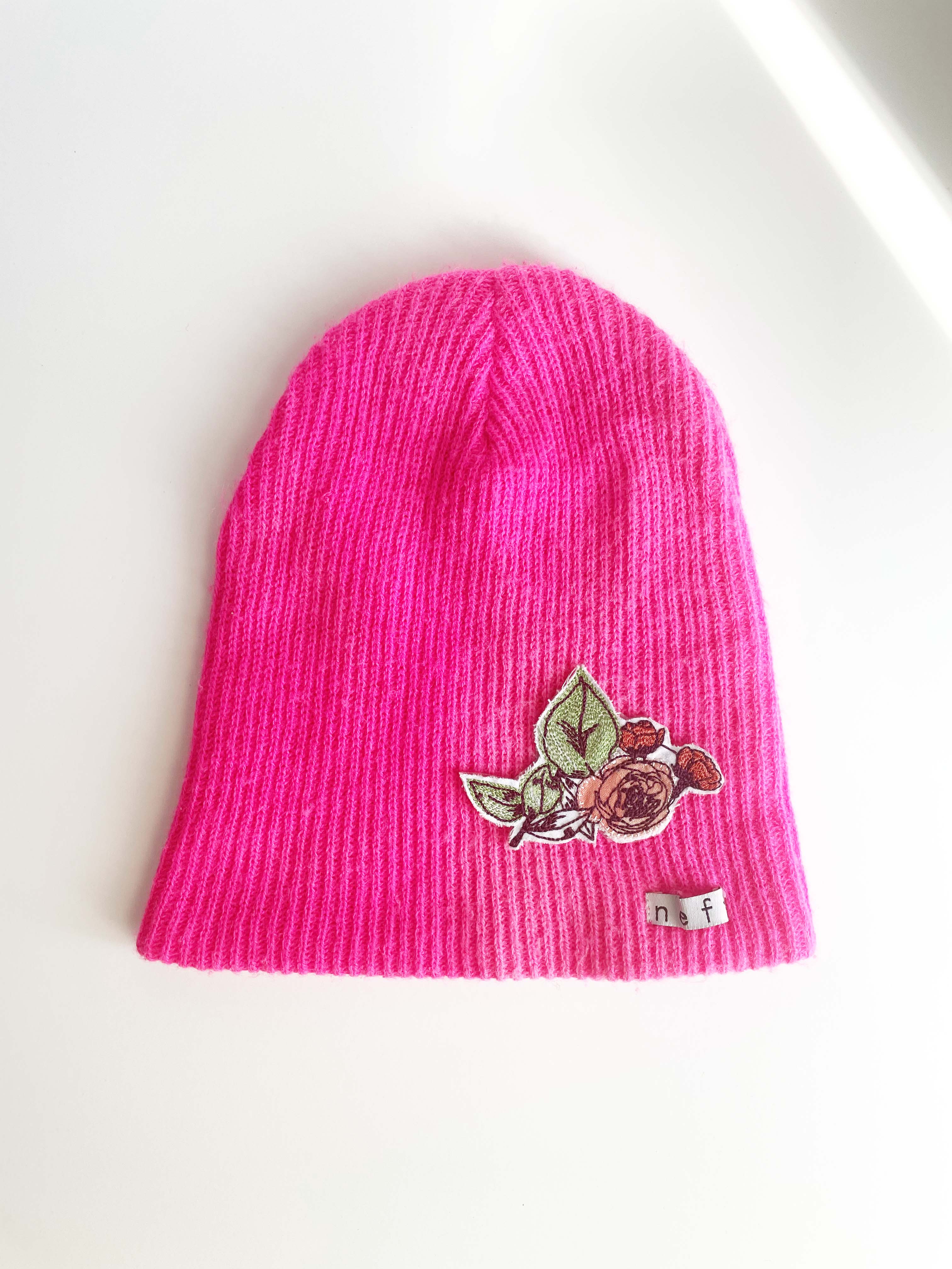 Hot pink knit hat with rose bush applique on bottom right. 