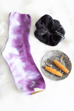 Load image into Gallery viewer, Purple dyed socks, black velvet hair scrunchie, wooden earrings on a ceramic holder sit on faux fur. 
