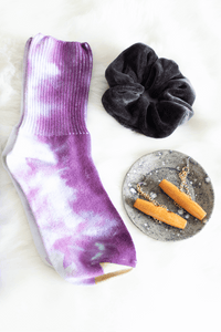 Purple dyed socks, black velvet hair scrunchie, wooden earrings on a ceramic holder sit on faux fur. 