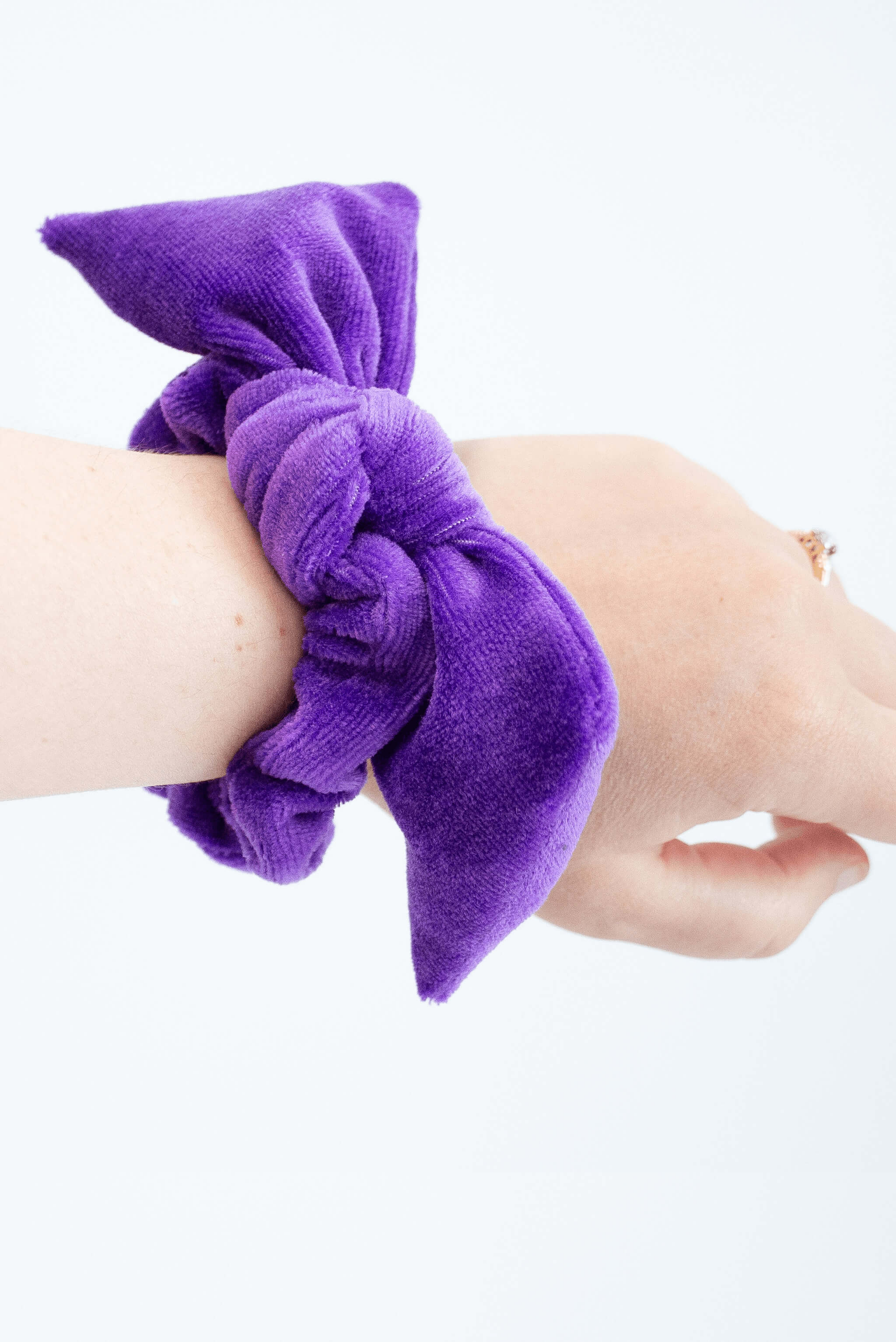 Purple velvet bow scrunchie worn on woman's wrist. 