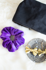 Load image into Gallery viewer, Zippered pouch with purple velvet hair scrunchie and gold bow earrings on ceramic tray. 
