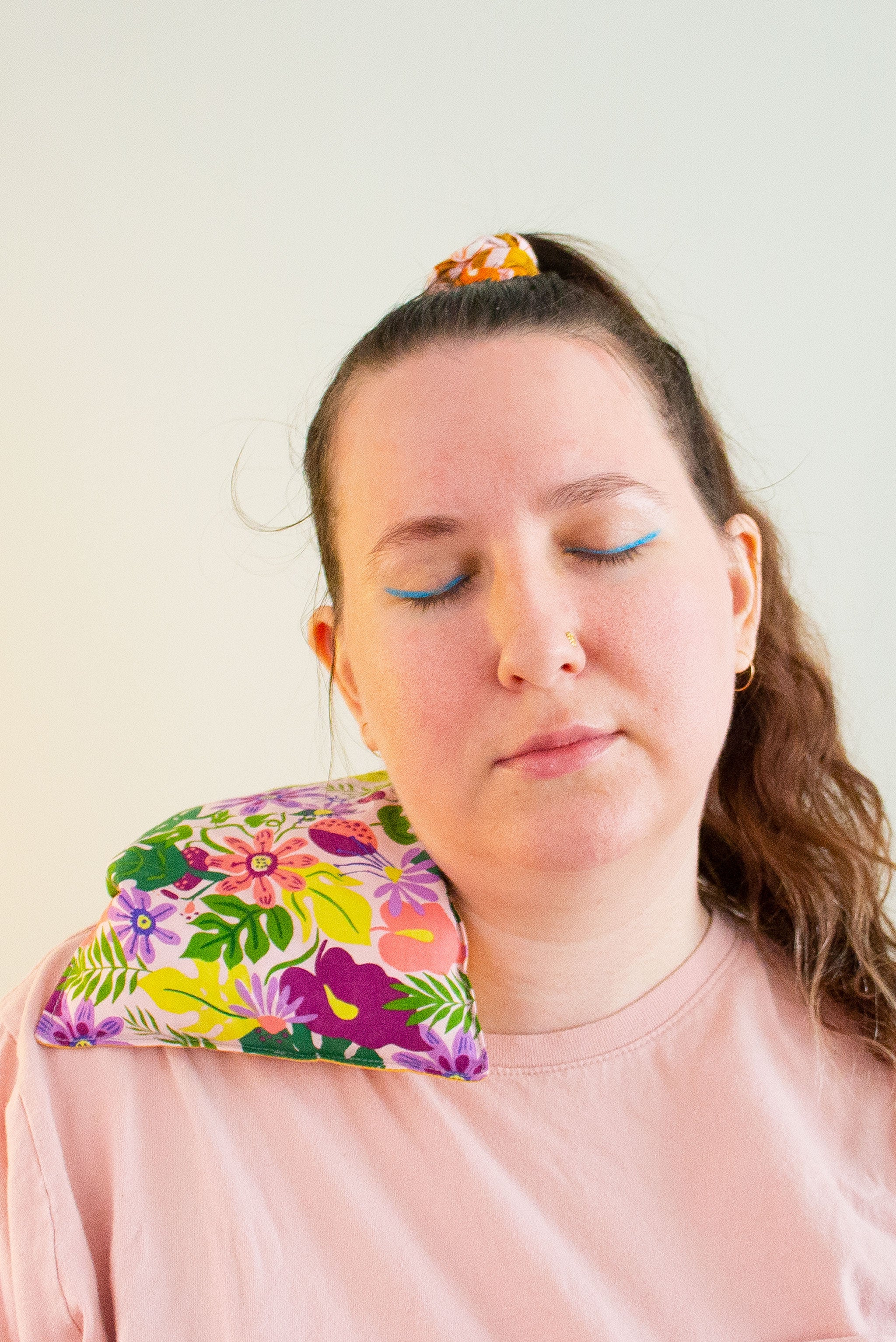 Woman with eyes closed and tilted head has a cherry pit grain bag draped across her right shoulder. 