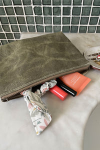 Zippered pouch on porcelain sink with hair scrunchie and makeup containers falling out of the bag. A small ceramic tray holds pairs of earrings. 