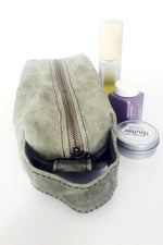 Load image into Gallery viewer, small waxed canvas toiletry bag with handle and brass zipper. The bag is closed and sits next to three small bottles and containers. The bag is sage green. 
