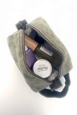 Load image into Gallery viewer, small waxed canvas toiletry bag with handle and brass zipper. The bag is open and contains small toiletries inside. The bag is sage green. 
