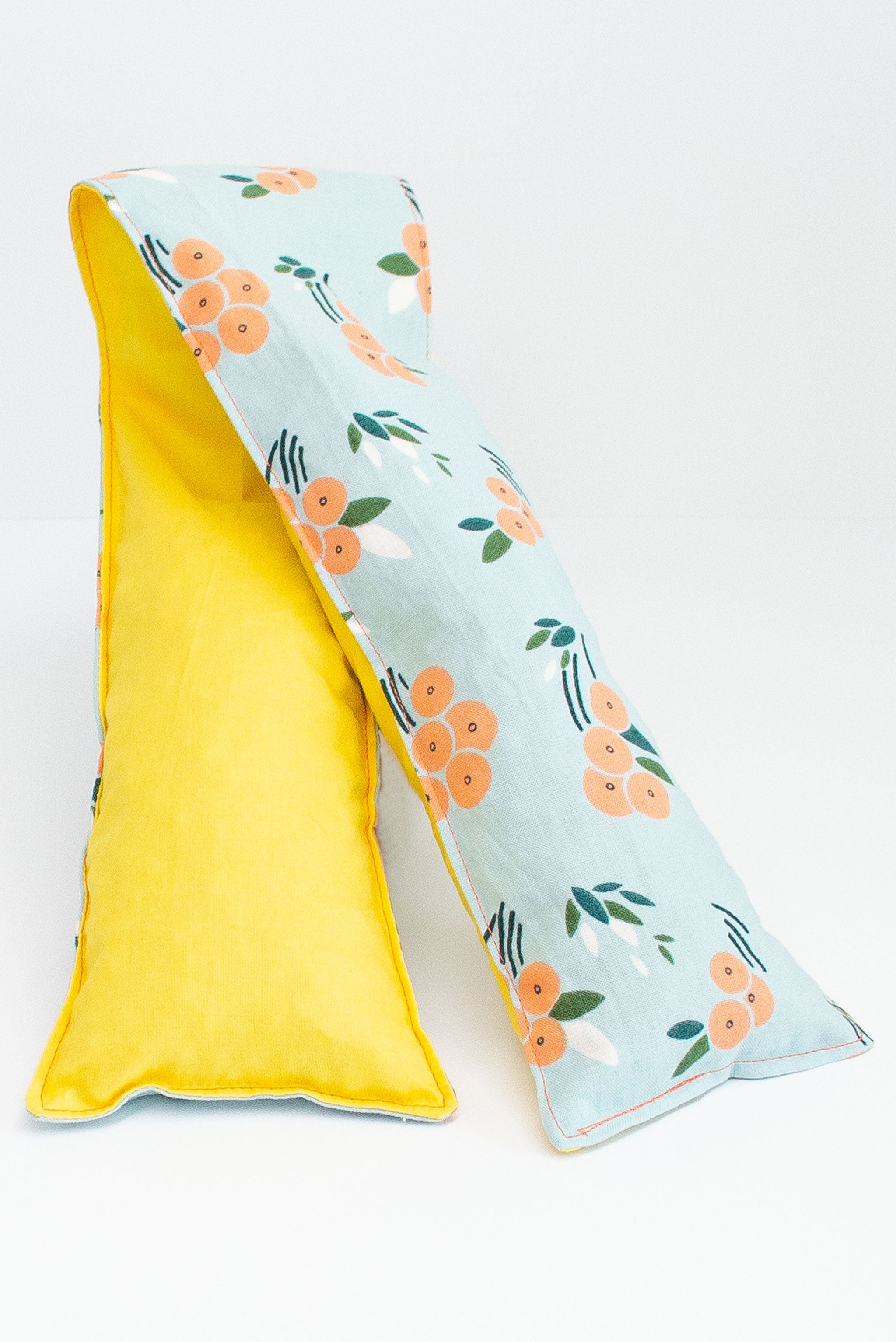 Long and skinny cherry pit grain bag on white background. Half yellow, half peach floral print on blue background. 