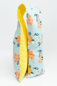 Long and skinny cherry pit grain bag on white background. Half yellow, half peach floral print on blue background. 