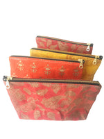 Load image into Gallery viewer, A row of waxed zippered pouches with brass zippers. From the back: red, yellow, red, and orange.
