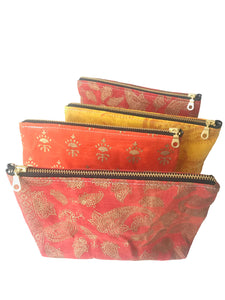 A row of waxed zippered pouches with brass zippers. From the back: red, yellow, red, and orange.