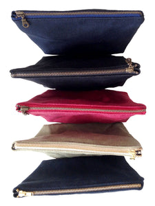 Row of 5 waxed zippered pouch with brass zippers. From the top: navy blue, black, red, sage green, and black again. 